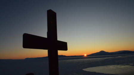 The wooden cross at the top of Observation Hill in Antarctica is silhouetted against a sunset in the distance.