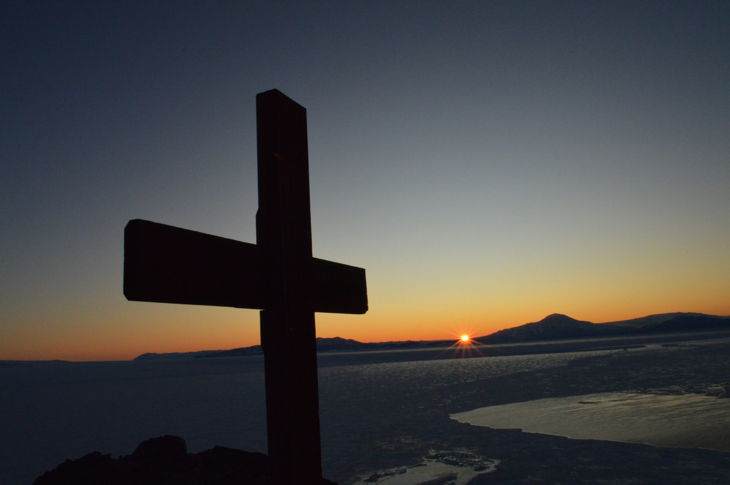 The wooden cross at the top of Observation Hill in Antarctica is silhouetted against a sunset in the distance.