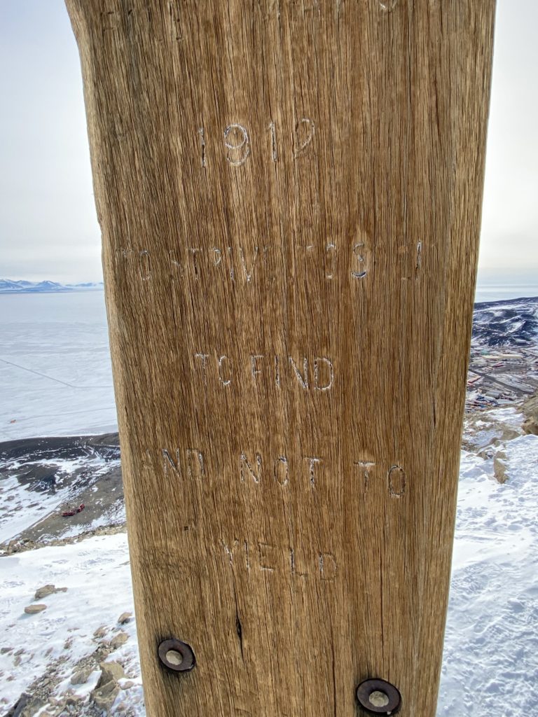 A close up look at the faded inscriptions on the cross, reading: 1912 TO STRIVE, TO SEEK TO FIND AND NOT TO  YIELD