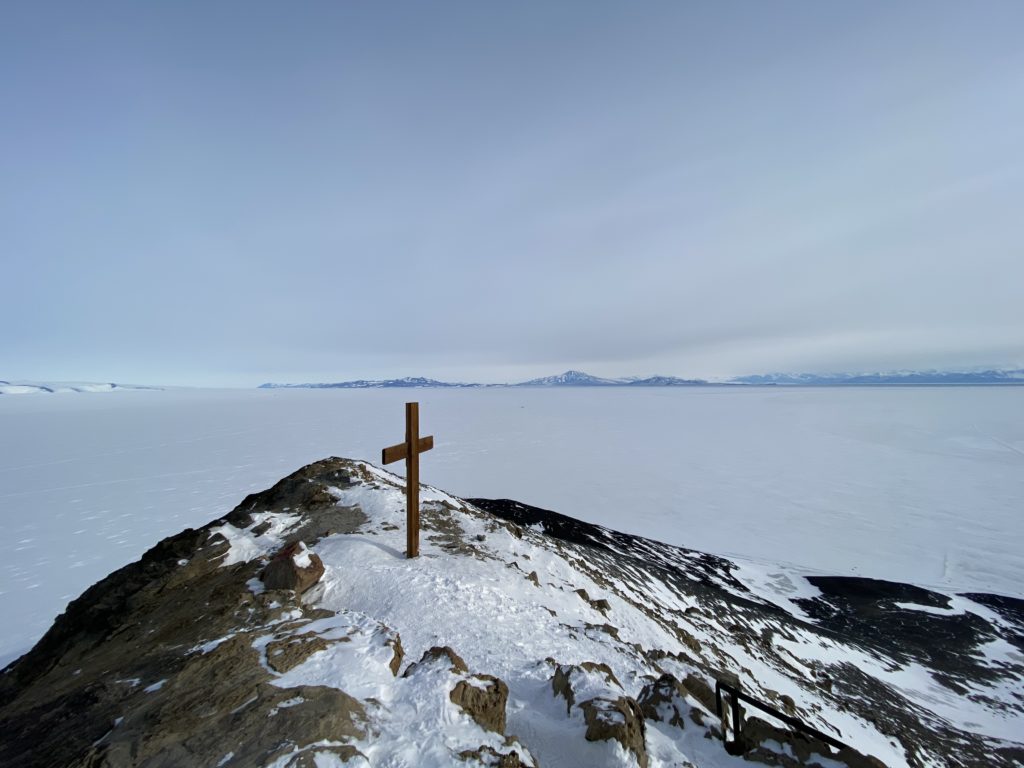 The wooden cross stands on Observation Hill, behind it is a sea of ice and pale blue skies.