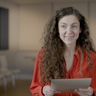 Yelena Akhtiorskaya, wearing a red top, holds paper in her hand as she speaks.