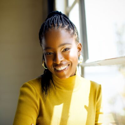 Amanda Gorman folds her arms and smiles while wearing a yellow long-sleeved top