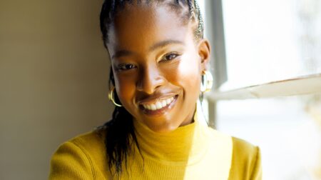 Amanda Gorman folds her arms and smiles while wearing a yellow long-sleeved top