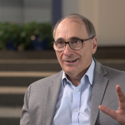 David Axelrod, wearing a suit, gestures with his hand as he speaks.