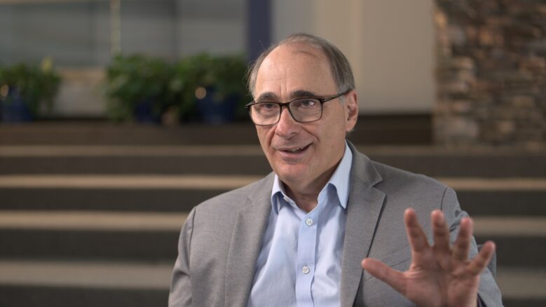 David Axelrod, wearing a suit, gestures with his hand as he speaks.