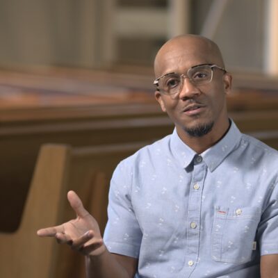 Daaron Battle, wearing a blue button-up, gestures with his hand as he speaks.