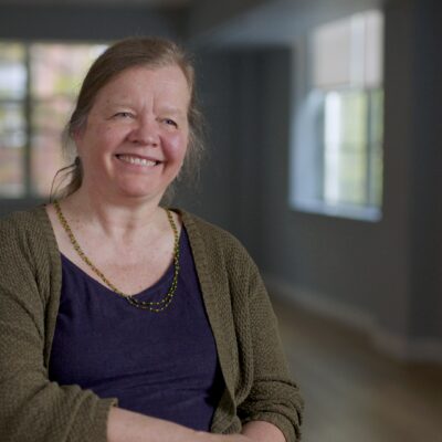 Ann Kjellberg, wearing a shirt and cardigan, smiles