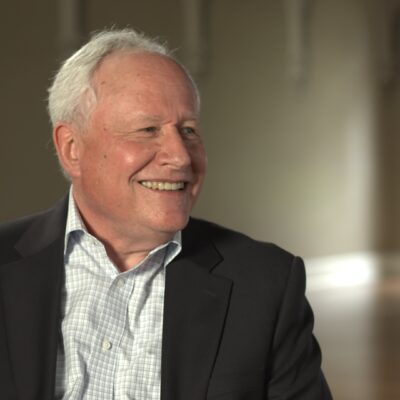 Bill Kristol, wearing a suit, looks to the side and smiles