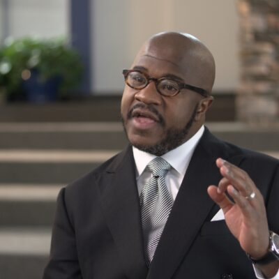 Pastor Terry E. Mackey, wearing a suit, gestures with his hand as he speaks.