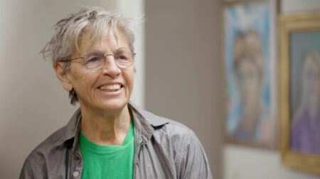Eileen Myles smiles while wearing a green shirt and gray jacket