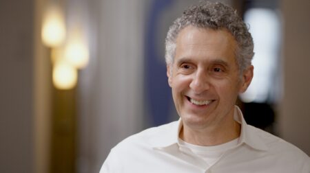 John Turturro smiles while wearing a white collared shirt