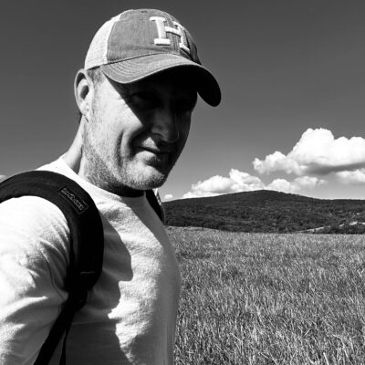 Jason Adam smiles while wearing a hat and standing in front of a grassy field