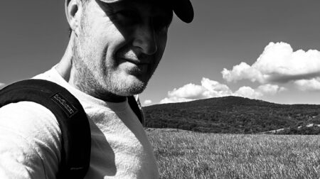 Jason Adam smiles while wearing a hat and standing in front of a grassy field